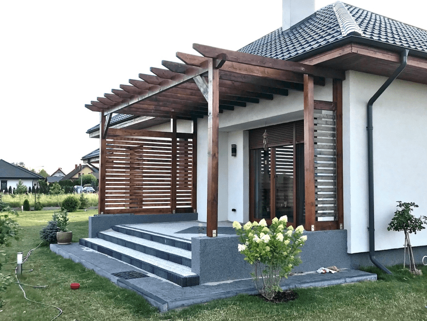 Taras wykonany przez firmę drewbon - stolarstwo ogrodowe. Taras ma schodki, szarą podłogę, a fundamenty ma brązowe